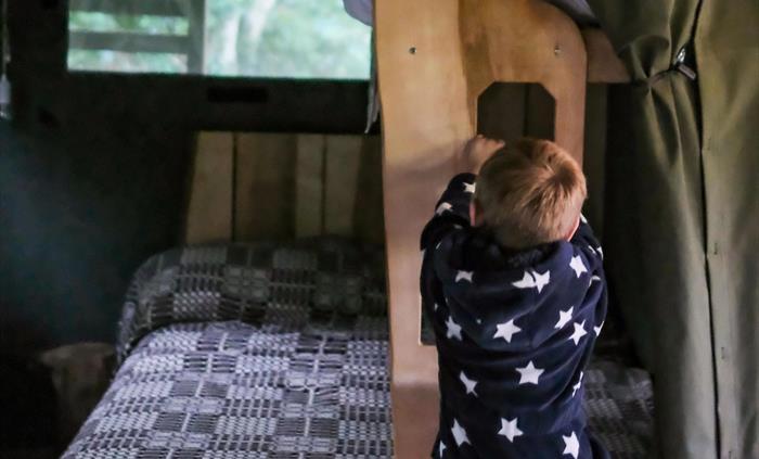 A child climbing up into a bunkbed in a safari tent.